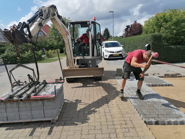 Medarbejdere lægger belægningssten med minigraver