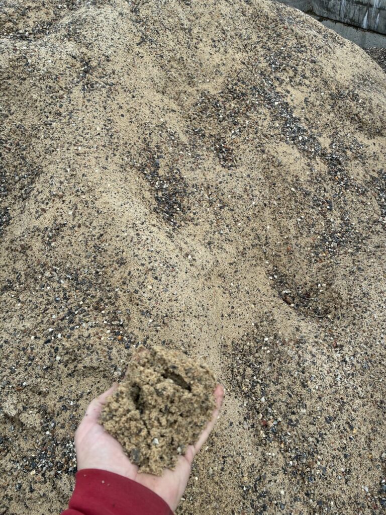 En håndfuld sand med fine småsten foran bunken